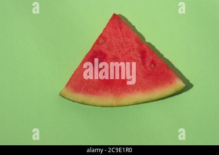 Flat lay of a green surface where a slice of red watermelon illuminated by direct sunlight is isolated Stock Photo