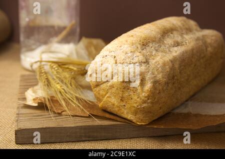 A loaf of homemade whole wheat bread next to a wheat branch and on a wooden board Stock Photo