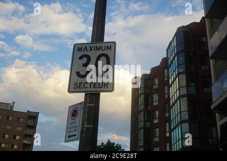 A traffic sign speed limit of 30 Km/hr in a sector with a background of a cloudy blue sky. No stop sign to the left says a bus stop from 5:30 am to 8: Stock Photo