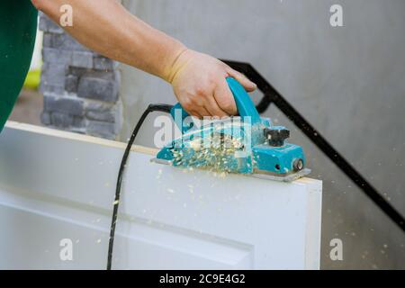 Professional using equipment carpenter maker hand tools on electric planer for processing wooden door Stock Photo