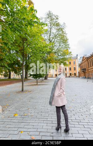 Happy young beautiful blonde woman walking along peaceful city plaza Stock Photo