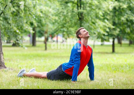 Yoga man in cobra upward facing dog pose stretching abs stomach muscles. Fit male sports model doing stretching exercise outdoor in summer on green gr Stock Photo