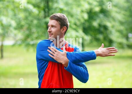 Front view of a sportsman stretching hands while standing outdoor in a park and looking by side. The concept of an active and healthy lifestyle Stock Photo