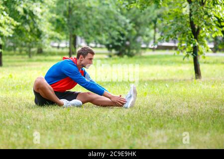 Man stretches muscles outdoor after hwaevy workout in public park. Concept of an active lifestyle and healthy lifestyle. Stock Photo