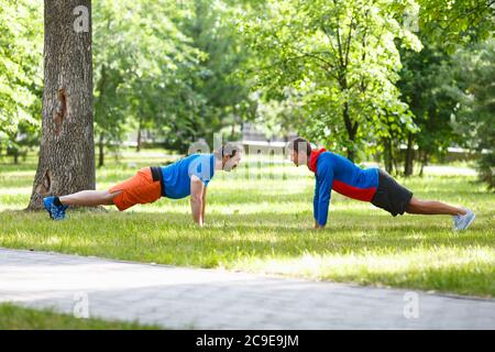 Two men do push-ups opposite each other in a public park. Active and healthy lifestyle concept. Selective focus. Stock Photo