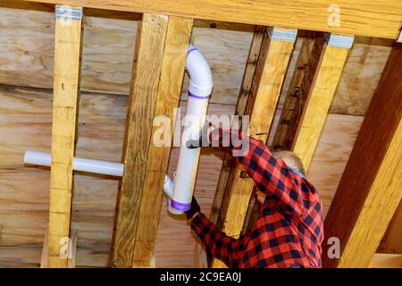 PVC plastic sewer toilet white pipe in the plumber gluing, on wooden frame ceiling beam of house soft focus Stock Photo