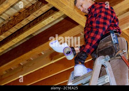 Plumber gluing PVC plastic sewer toilet white pipe on wooden frame ceiling beam of house soft focus Stock Photo