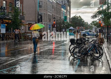 Montreal, CA - 30 July 2020: Woman on Mont-Royal Avenue holding rainbow umbrella during rain & storm Stock Photo