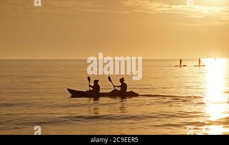 Portobello, Edinburgh, Scotland, UK. 31 July 2020. Sun was slow to appear from behind the clouds at dawn with temperature of 12 degrees. Forecast is for the mid to high twenties today. Pictured: Two girls in a kayak and paddle boarders enjoyed the sunrise activity. Stock Photo