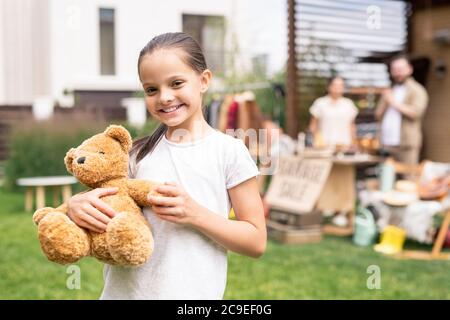 Portrait of smiling pretty girl embracing toy bear bought at garage sale Stock Photo