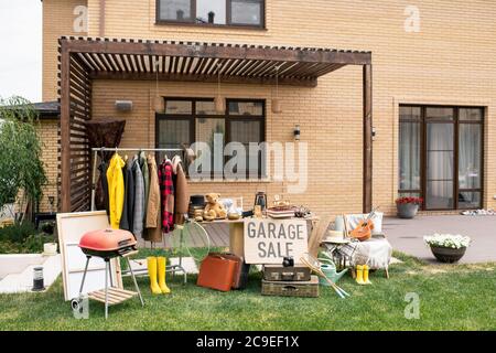 Garage sale sign placed at table with unique goods in backyard of beautiful brick house Stock Photo