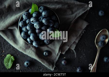 Top down view of the fresh blueberries. Group of organic blueberries with mint leaves, in dark bowl, on top of dark wooden board. Stock Photo
