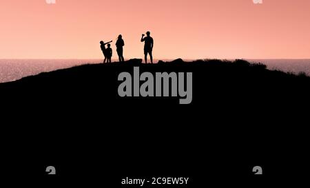 A panoramic view of a family of holidaymakers standing on the top of the remains of a Bronze Age barrow on Pentire Point East in Newquay in Cornwall. Stock Photo