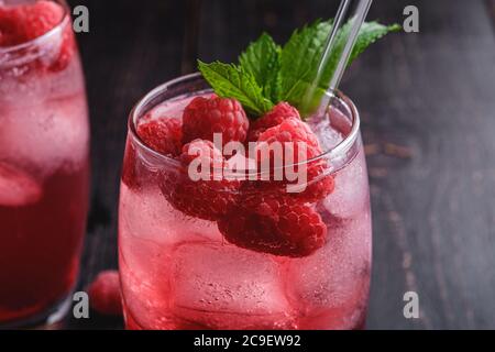 Fresh ice cold berry juice drink with mint, summer raspberry lemonade in glass with straws on dark wooden background, angle view macro Stock Photo