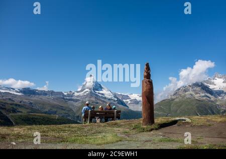 Family enjoying a picnic against the backdrop of the Swiss Alps. View from the Five Lakes walking trail in Zermatt. Stock Photo