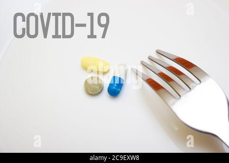 Pills and capsules with a fork on a white background - food, protection against influenza during quarantine, coronavirus, lettering covid19 Stock Photo
