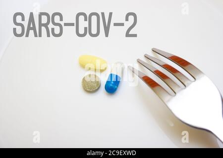 Pills and capsules with a fork on a white background - food, protection against influenza during quarantine, coronavirus, covid19, lettering sars-cov- Stock Photo
