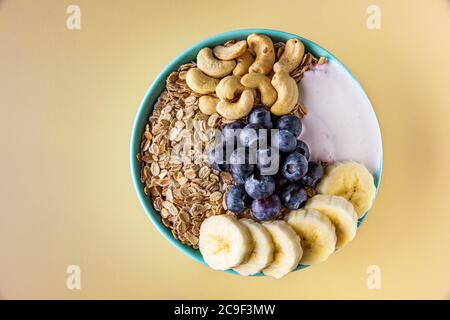 Healthy breakfast with yogurt, cereal, and ripe fruit served in blue bowl. Isolated on light yellow background. Stock Photo