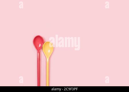 Two plastic colored spoons on a pink background Stock Photo