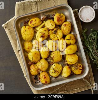 Oven baked whole crushed and crusty potato spuds with seasoning and herbs in metalic tray. Stock Photo