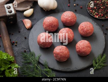 Raw fresh minced beef meatballs on round board with pepper,garlic and parsley on black table background. Stock Photo