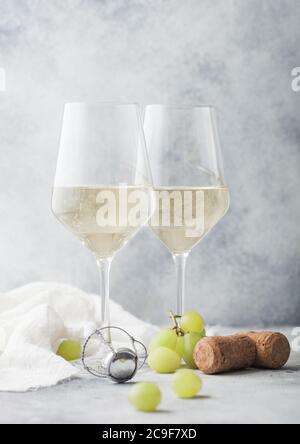 Two crystal glasses of white homemade wine with corks and grapes on light table background. Stock Photo