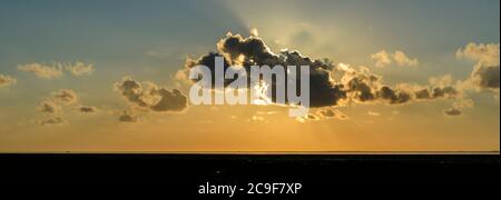 Clouds with sun rays during sunset over the Wadden Sea on the north Dutch coast. Stock Photo
