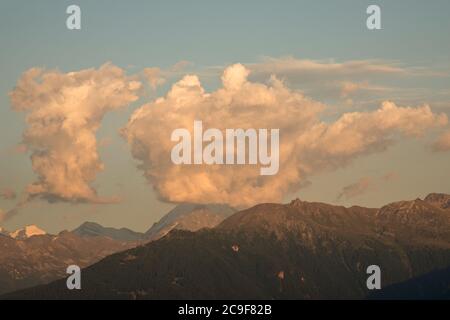 Unusual cloud shapes above mountains. Golden evening light with strong colours and textures in the cloud. Blue sky behind the clouds. Stock Photo