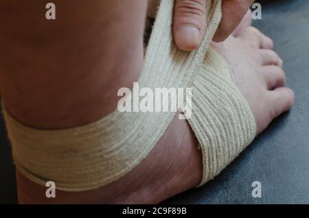 Middle-aged Caucasian man produces an independent bandage of his dislocated leg. He puts an elastic bandage over his swollen shin. First aid in sprain Stock Photo