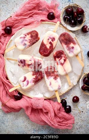 Fresh cream and cherry homemade popsicles placed on white ceramic plate with fruits and textile Stock Photo