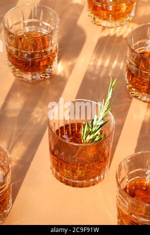 Many glasses of cold whiskey served in rocks with rosemary on beige trendy background. Vertical format. Stock Photo