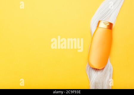 Shampoo bottle mock up on lock of blonde hair on orange color background. Gold bottle shampoo in dyed hair strand. Hair care cosmetics bath beauty Stock Photo