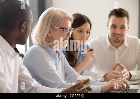 Mature businesswoman coach teaching diverse employees, using laptop Stock Photo