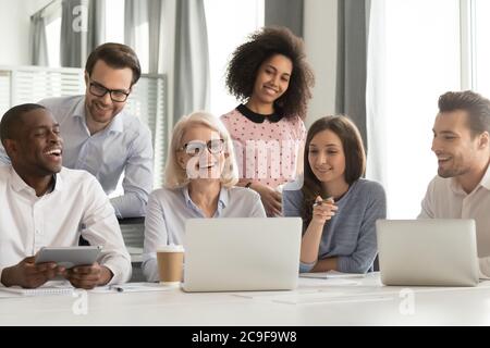 Smiling mature mentor teaching diverse employees team, using laptop Stock Photo