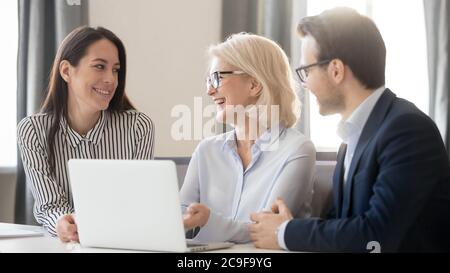 Happy employees interns discussing new corporate software, using laptop Stock Photo