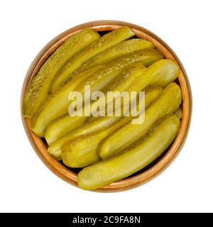 Sliced pickled cucumbers, also known as pickle or gherkin, in a wooden bowl. Small pickled cucumbers with bumpy skin, sliced lengthways. Baby pickles. Stock Photo