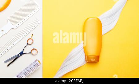 Gold shampoo bottle mock up on lock of blonde dyed hair strand on orange color background with set hairdresser tools equipment. Hair care cosmetics Stock Photo