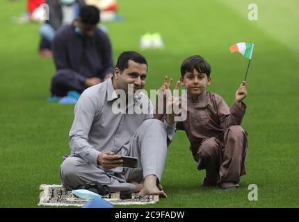 Kamil Ayub (right), aged 6, holds an Irish flag alongside his father (left) sitting on a prayer mat in Croke Park, Dublin, as mosques across Ireland are marking the occasion of Eid Al Adha, the festival of sacrifice - with the largest event taking place at GAA headquarters in Dublin. Stock Photo