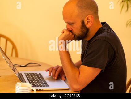Young white Caucasian man looking worried sitting at table with laptop computer, UK Stock Photo