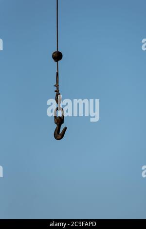 Close-up of black iron lifting hook attached to heavy duty wire cable hanging from crane in harbour next to Revier Tejo in Belem Portugal Stock Photo