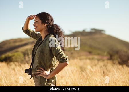 Side view of a woman on holiday standing near a hill looking around. Female photographer looking away standing outdoors on a sunny day. Stock Photo