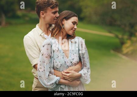 Man embracing his girlfriend from behind at the park. Affectionate couple at the park. Stock Photo
