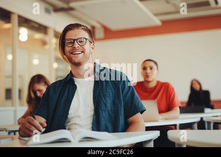 Portrait of young male student in high school classroom. Young man in colleague classroom looking at camera and smiling. Stock Photo