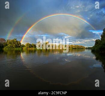 Double rainbow over river. It is reflected. Dramatic sky. Stock Photo