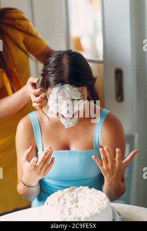 Young woman dips face in white cake with cream. Happy birthday concept.
