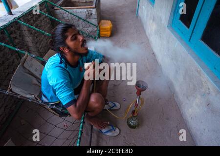Bodufolhudhoo / Maldives - August 17, 2019: young man with ponytail sitting smoking hookah at sunset Stock Photo