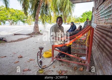 Bodufolhudhoo / Maldives - August 17, 2019: Maldivian man fixing traditional Maldivian bench made with ropes Stock Photo