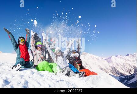 Group of young adults throw snow up in the air sitting on top of the mountain over sunny alpine peaks Stock Photo