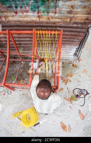Bodufolhudhoo / Maldives - August 17, 2019: Maldivian man fixing traditional Maldivian bench made with ropes Stock Photo