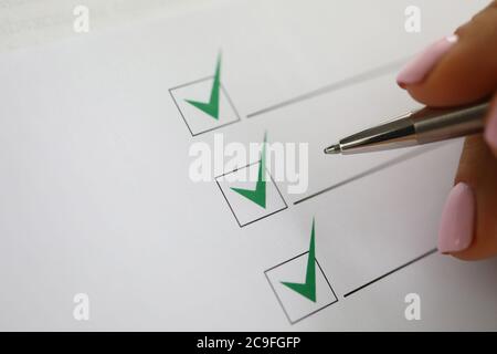 Woman's hand holds pen and marks green check marks in document. Stock Photo